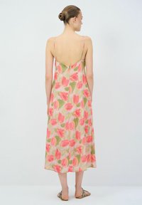 Bloemrijke maxi-jurk met verstelbare spaghettibandjes, met een roze en groene tulp patroon op een lichtbeige achtergrond, zachte stof, vloeiende silhouette.