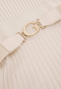 Tissu en maille côtelée beige avec une ceinture élastique assortie beige ornée d'une boucle "G" métallique dorée au centre.