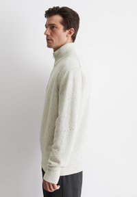 Helles beiges Strickpullover mit hohem Kragen, gerippten Bündchen und einem strukturierten Muster mit Sprenkeln. Weiches, lässiges Design.