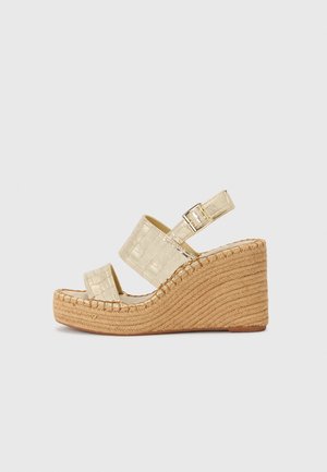 Beige kile-sandal med tekstureret platåsål, to brede remme med krokodillepræg og en justerbar ankelspænde.