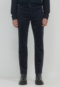 Pantalons en velours côtelé marine avec une coupe slim, dotés d'une fermeture à bouton, de cinq poches et d'une texture lisse. Portés avec des bottes en cuir noires.