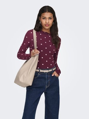 Langærmet bordeaux top med hvide polkaprikker, ribbet tekstur og en bølget halsudskæring, kombineret med mørkeblå vidde bukser og en beige taske.