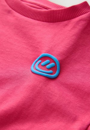 Lyserød bomulds-t-shirt med ribbet halsudskæring og et tekstureret blåt logo på venstre bryst, der har en cirkulær form og bøjede linjer.