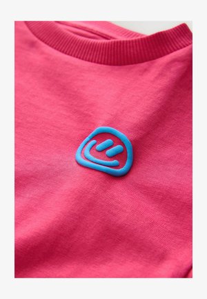 Różowy bawełniany t-shirt z prążkowanym kołnierzem i fakturowanym niebieskim logo na lewej piersi, o okrągłym kształcie i zakrzywionych liniach.