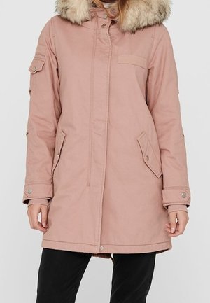 Femme portant un manteau d'hiver rose clair avec un grand col en fourrure beige, des poches à rabat et des poignets à boutons-pression.