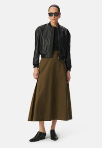 Zwarte leren bomberjack over een aansluitend zwart topje, gecombineerd met een olijfgroene midi-jurk en zwarte blokhak muiltjes.