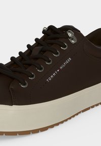 Σκούρο καφέ αθλητικό παπούτσι Tommy Hilfiger με μαύρα κορδόνια, ασημένιες ρυγές και παχύ, εκρού πέλμα με υφή και καφέ πάτο.
