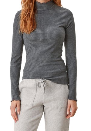 Frau trägt ein eng anliegendes, dunkelgraues, geripptes Langarmshirt mit gewellten Kanten und hellgraue Sweatpants mit Kordelzug.