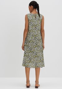 Ärmelloses Kleid mit tailliertem Oberteil und weit schwingendem Rock; verfügt über ein florales Muster in Grün, Schwarz und Weiß; Rückenteil mit Schlüsselaugen-Design.