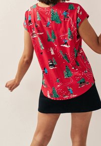 Maglietta rossa a maniche corte con stampa a tema invernale che include alberi, pupazzi di neve e sciatori. Tessuto morbido, vestibilità comoda e scollo rotondo.