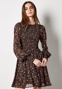 Czarna sukienka w kwiaty z marszczonym przodem, długimi bufkami i rozkloszowanym dołem, zdobiona czerwonymi, zielonymi i żółtymi wzorami kwiatowymi.