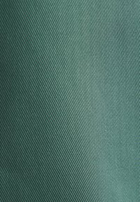 Tessuto turchese con una trama a coste diagonali, che mette in risalto una superficie liscia e un colore ricco e vibrante.