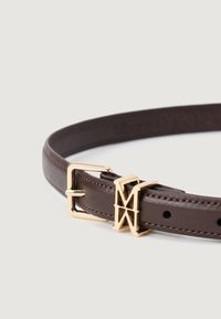 Rudas odinis diržas su lygiu paviršiumi, turintis auksinės spalvos sagtį ir logotipo akcentą. Užbaigtas kontrastingos siūlės detalėmis.