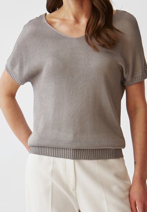 Pull léger gris clair à manches courtes avec un col en V, ourlet côtelé et motif de tricot texturé. Associé à un pantalon blanc pour un look contrastant.