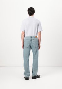 Svetlo modri jeans z ravnim krojem, ki imajo rjav usnjen znak na zadnjem pasu. Mehka pletena polo majica v svetlo sivi barvi.