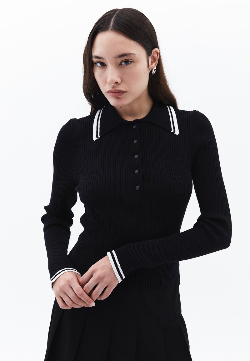 Svart långärmad polo med ribbad yta, knäppning vid halsen, vitrandig krage och manschetter, som har en figurnära silhuett och texturerat tyg.