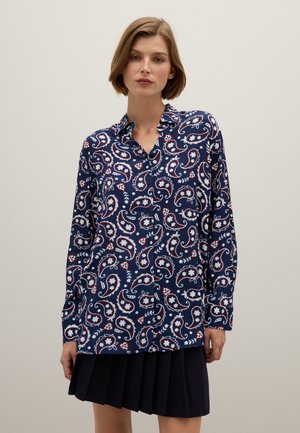 Camisa de manga larga azul marino con estampado de cachemira y flores, con cuello abotonado y un ajuste relajado, combinada con una falda oscura con pliegues.