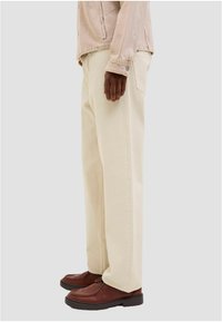 Bež hlače širokih nogavica od pamuka s glatkom teksturom, uparene s smeđim cipelama na vezanje i svijetlom jaknom.