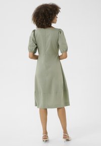 Olive zeleno midi obleko s napihnjenimi rokavi, visokim ovratnikom in oprijetim pasom. Gladka tekstura s razporkom na hrbtni strani.