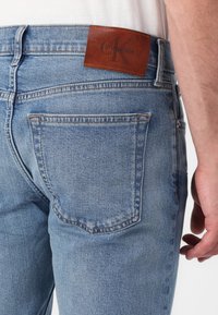Blaue Denim-Jeans im Slim-Fit, mit einem braunen Lederpatch von Calvin Klein am hinteren Bund und an den Gesäßtaschen.