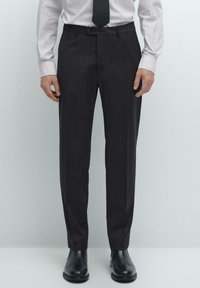 Dark pinstriped trousers made of fabric, featuring a slim fit, flat-front design, and a button closure, paired with black leather shoes.