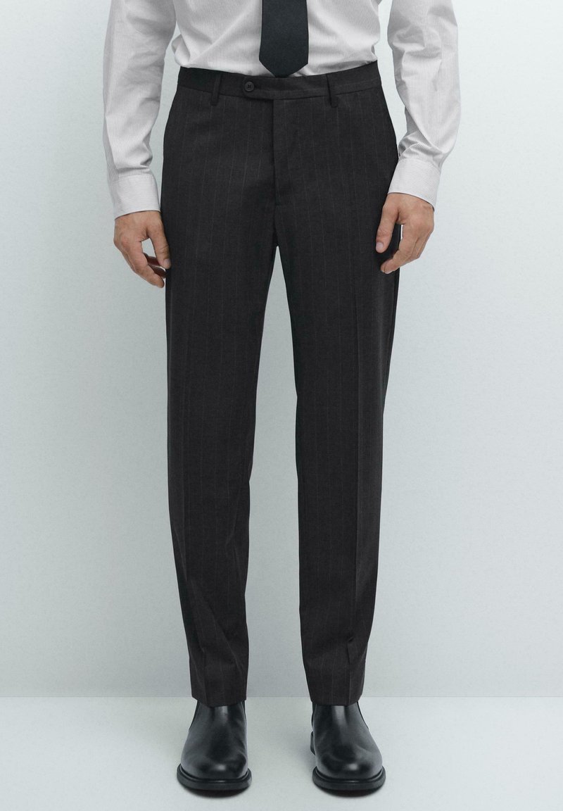 Dark pinstriped trousers made of fabric, featuring a slim fit, flat-front design, and a button closure, paired with black leather shoes.