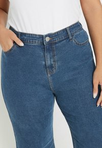Blauwe spijkerbroek met een hoge taille, voorzakken en een knoopsluiting. Heeft subtiele vervaging en contrasterende stiksels langs de naden.