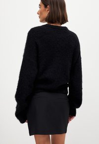 Mustat karheat neuleet, joissa on pudotetut olkapäät, yhdistetty mustan istuvan hameen kanssa. Ominaisuuksia ovat ribbireunat hihansuissa ja helmassa. Minimalistinen muotoilu.