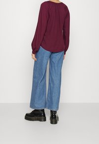 Maglia a maniche lunghe color marsala con dettagli arruffati nel scollo, abbinata a jeans in denim blu a gamba larga e calzature platform nere.
