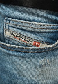 Μικρή φθαρμένη τσέπη από μπλε τζιν με ετικέτα υφάσματος «Diesel Industry» ραμμένη στην επάνω άκρη της τσέπης.