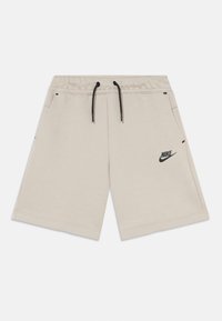Beige cotton shorts with an elastic waistband and black drawstring, featuring side pockets and a black Nike logo on the left side.