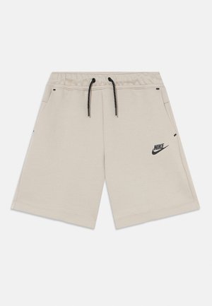 Shorts en coton beige avec une taille élastique et un cordon noir, dotés de poches latérales et d'un logo Nike noir sur le côté gauche.