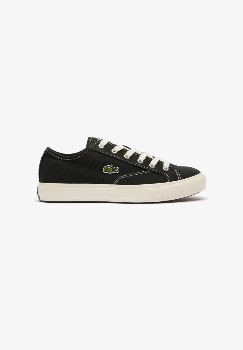 Baskets basses noires avec lacets et semelle blanches, arborant un logo crocodile vert sur le côté et des détails de coutures blanches.