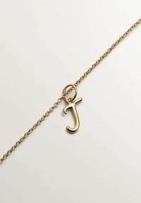 Collar de cadena de oro con un pequeño colgante en forma de letra "J" sobre un fondo claro y liso.
