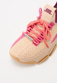 Zapatilla beige texturizada con acentos en rosa, cordones gruesos y suela de goma. Presenta un logo en la lengüeta y una parte superior tejida distintiva.