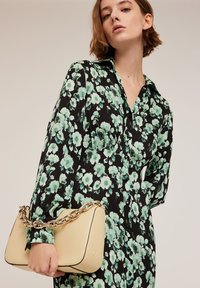 Abito nero a fiori con fiori verdi, con bottone sul davanti e maniche lunghe. Borsa beige con manico a catena, texture liscia e forma tondeggiante.