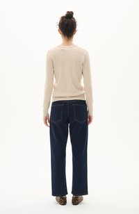 Maglione beige a coste con maniche lunghe abbinato a jeans a gamba larga blu scuro. Scarpe con stampa leopardo marrone molto evidenti. Vista frontale non visibile.