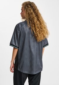 Szary sweter wykonany z lekkiego materiału, z teksturowanym wzorem w zygzak, krótkimi rękawami i kontrastującymi paskami w kolorze czarnym i teal na mankietach.