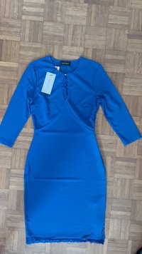 Blaues, figurbetontes Kleid mit langen Ärmeln, ausgestattet mit einem Schlüssel-Ausschnitt, Spitzenverzierungen und einem gewellten Saum. Hergestellt aus einem glatten, glänzenden Stoff.
