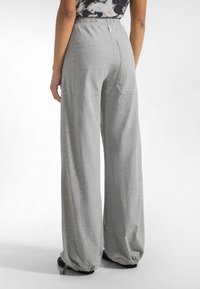 Pantalones de pierna ancha en gris claro con una textura suave, con una cinturilla alta y dos bolsillos traseros. Puños elásticos en los tobillos completan el diseño.