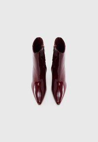 Bottines à talons pointus de couleur rouge foncé brillante avec fermetures éclair latérales, vues de dessus sur un fond blanc.