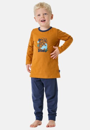 Langärmliges orange Baumwollhemd mit blauen Akzenten, das ein Dinosaurier-Motiv zeigt; kombiniert mit dunkelblauen Baumwollhosen mit Umschlägen.