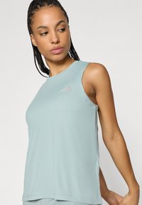 Hele sinine varrukateta sportlik särk siledas, tekstuurse kangaga, ümar kaelusega ja väikese logoga rinnal.