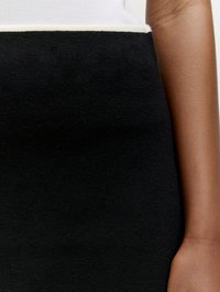Zwarte gebreide rok met een witte bies aan de taille, die een soepele textuur en een figuuraccentuerend ontwerp laat zien. Close-up van de stof en hand.