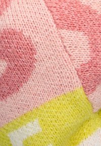 Närbild av mjukt stickat tyg med rosa, ljusrosa och gula geometriska mönster med synlig stickstruktur.