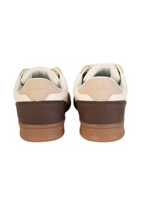 Białe i brązowe sneakersy z gładką skórzaną cholewką, teksturowaną ciemnobrązową podeszwą i subtelnym logo na pięcie.