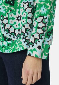 Kleurige blouse met een levendig groen, zwart en blauw abstract bloemmotief; zachte stof; lange mouwen; ontspannen pasvorm.
