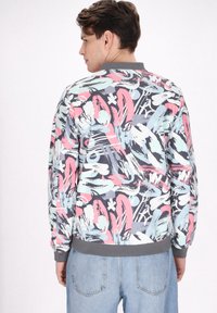 Jachetă bomber colorată cu un model abstract în nuanțe de roz, albastru deschis și gri, cu guler și mansete ribbonate gri.