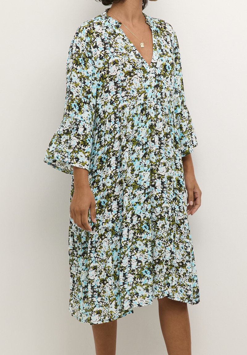 Robe fleurie avec un décolleté en V, des manches cloche et une coupe ample. Le motif présente des bleus, blancs et verts sur un fond noir. Longueur midi.