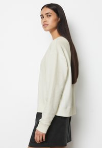 Pullover beige chiaro con polsini e orlo a costine, vestibilità rilassata e texture morbida; abbinato a una mini gonna nera.